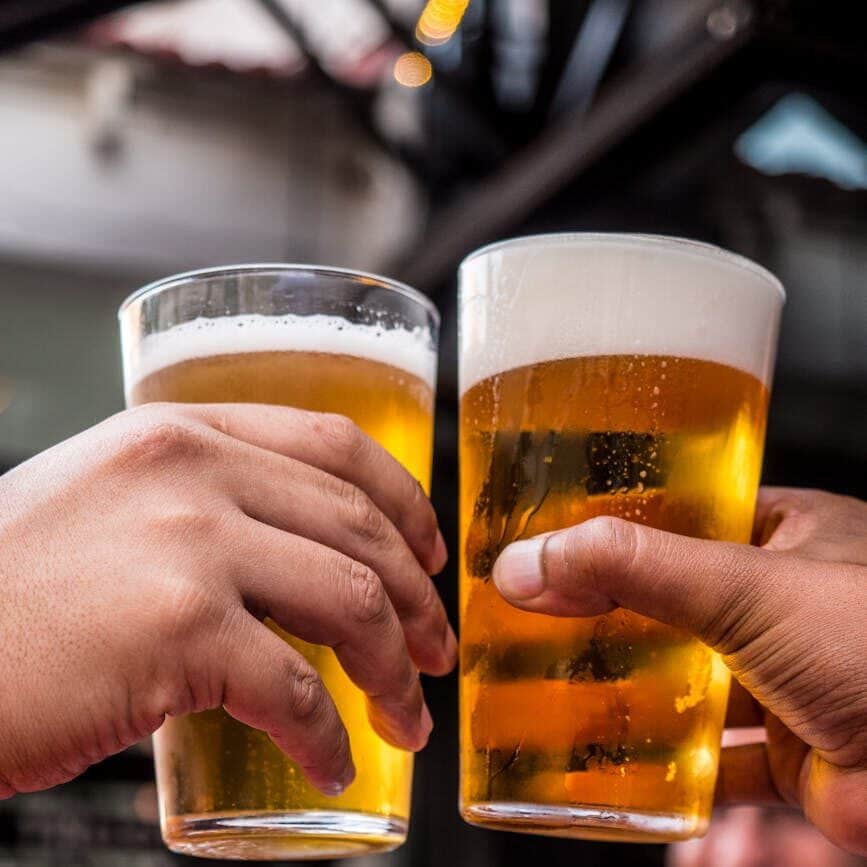 two persons holding drinking glasses filled with beer